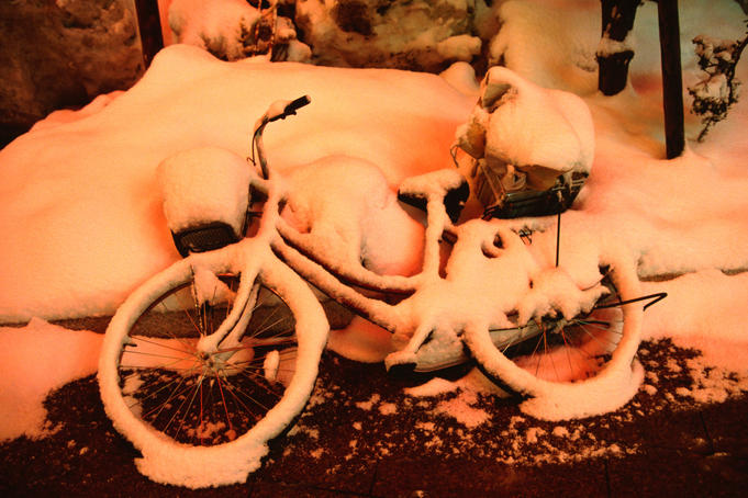 An abandoned bicycle under snow, painted with a red glow from neon in the entertainment quarter in Susukino.