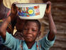 A young Gourmantche girl holding a decorated Nigerian bowl on her head.