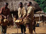 Three traditional drummers playing for acrobats and a stilt-dancer in the village of Zala.