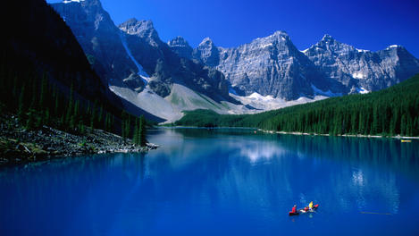 People paddling their canoe on the impossibly blue waters of Moraine Lake, surrounded by the Rocky Mountains in the Banff National Park.