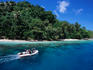 Divers in a small boat travel past an island beach.