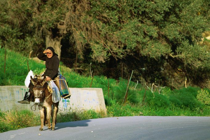 Elderly Cretan in the traditional black clothing riding sidesaddle on a donkey - Crete