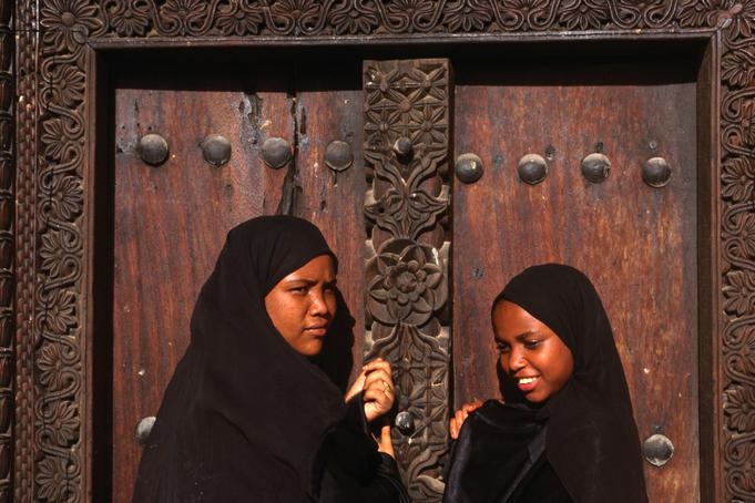 Young Islamic girls in traditional bui-bui stand in front of a typical Zanzibar doorway in Lamu.