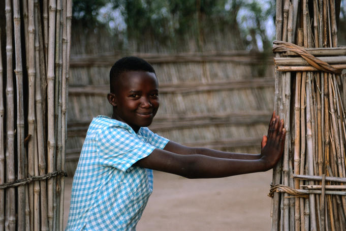 A woman standing at the entrance gate of a homestead.