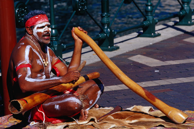 Australian Aboriginal busker playing didgeridoo in central city.