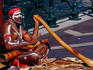 Australian Aboriginal busker playing didgeridoo in central city.