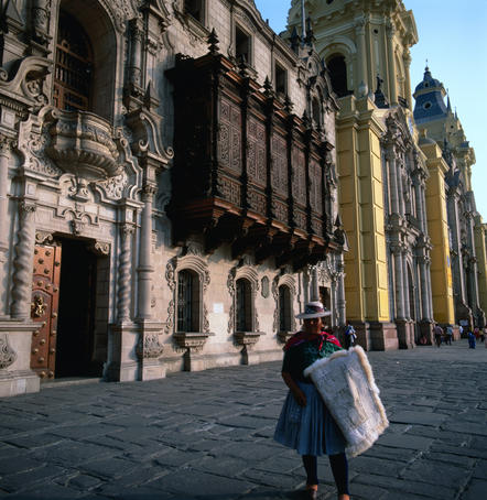 A Quecha lady standing in front of the Archbishop's Palace and Colonial Cathedral of Lima.