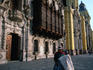 A Quecha lady standing in front of the Archbishop's Palace and Colonial Cathedral of Lima.