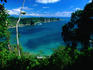 Looking through trees and across a clear water bay, to a rocky peninsula