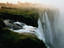 Water vapour from the foot of a waterfall rises to greet the head of the falls, where a river cuts through grasslands