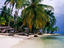 Idyllic beach scene: a woman relaxes in a hammock in front of a thatched bungalow.