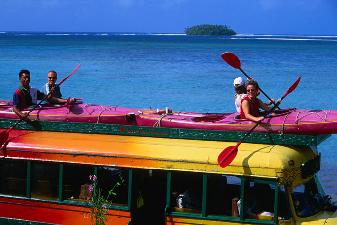 Tourists hitch a ride in a kayak on the roof of a tour bus.