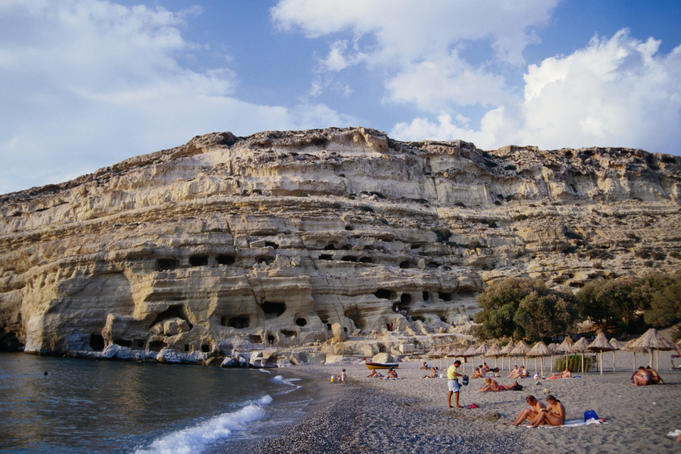 People sun-bathing on the sheltered beach at Matala. The beach is edged by cliffs sporting man-made caves that date back to prehistoric times.