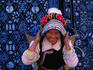 A Bai woman carrying a basket on her back stands in front of a colourful batik piece.