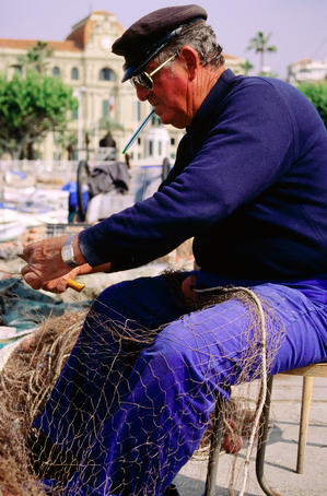 Fisherman mending net at harbour.