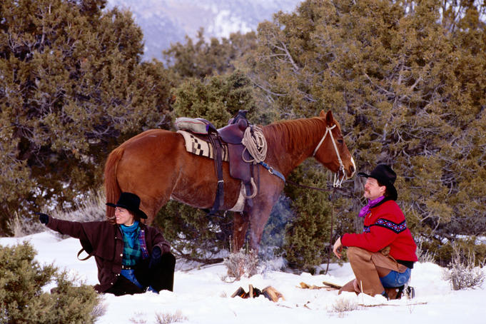 Cowboy, cowgirl and horse around fire in snow.