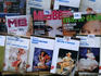 Glossy women's magazines and 1950's style erotic novels in kiosk window.