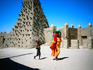 A woman in yellow robes, and a child walk past the Sankore mosque, built in the traditional Sahel style, using mud-bricks and wooden beams which stick out so that ladders can be propped against them when the time comes to repair the rendered walls - Timbuktu
