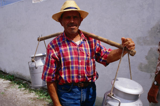 Man carrying milk churns across his shoulder.