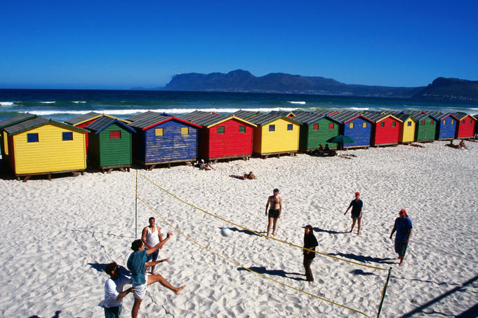Volleyball game next to beach huts.