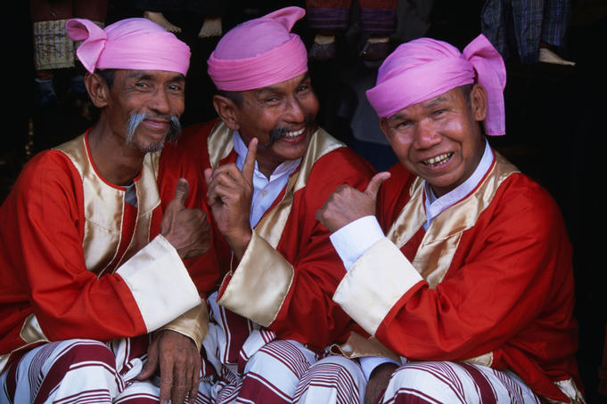 Three men in traditional clothing and headwear, known as the Moustache Brothers, giving the thumbs up