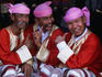 Three men in traditional clothing and headwear, known as the Moustache Brothers, giving the thumbs up