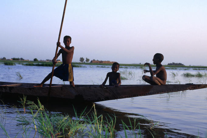 Three boys play on a canoe (pirogue) on the river in Mopti.