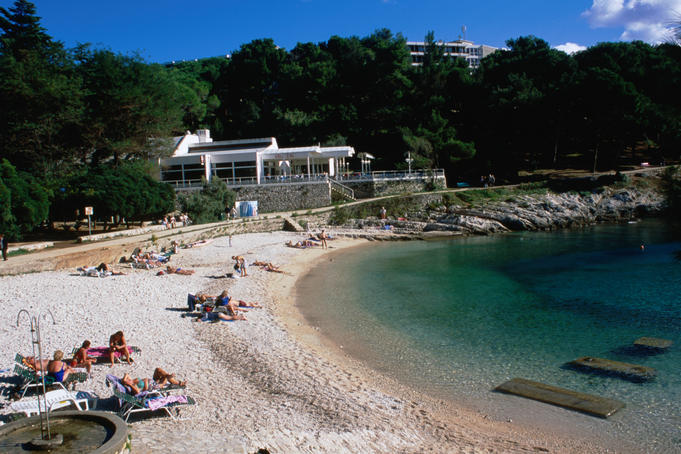 Tourists on sand beach surrounded by pine groves.