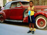 Young boy with hobby horse in front of old car.