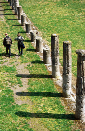 Couple walking past columns in Casermi dei Gladiatori, Old Pompeii.