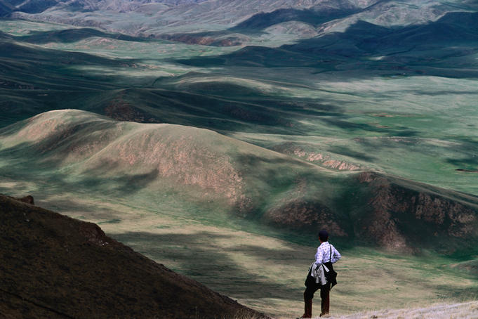 Trekker looking out at hills and meadows outside of Kochkor, Kyrgyzstan