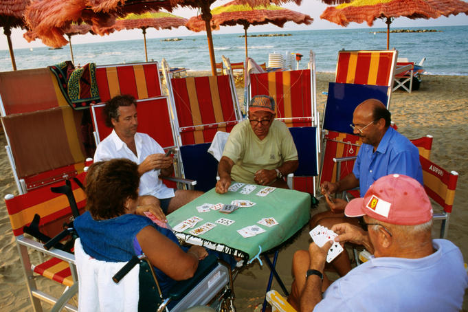 People playing cards under beach umbrella.