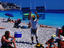 Man on beach holding up chairs for rent.