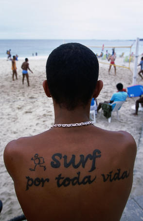 Boy with tatoo on back that reads "surf all life long" on Ipanema beach.