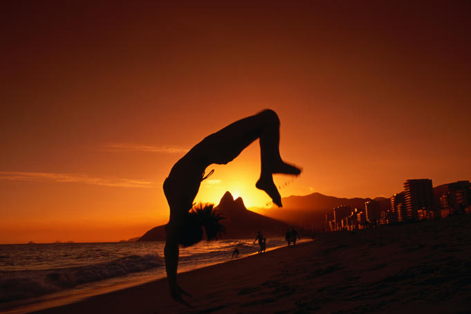Man doing somersault on beach at sunset.