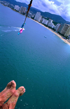 Sandy feet of parasailer and high angle view of city.