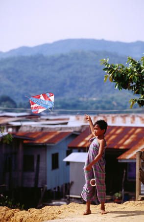 village boy flying kite over iron rooftops.
