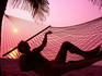 Man relaxing in hammock on beach at sunset.