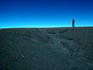 Man walking on rim of Irazu volcano crater, against blue sky.