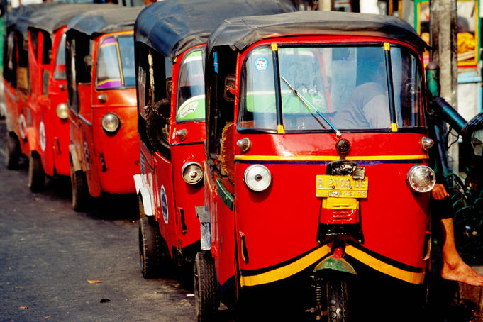 Three-wheeled Bajaj transportation lined up in street.