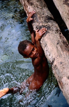 Young boy hanging from log in creek.