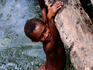 Young boy hanging from log in creek.