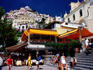 Tourists near waterfront restaurants with hillside houses in background.