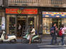 Woman on motorbike outside shop.