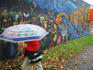Walking with umbrella past neighbourhood mural, Commercial Drive.