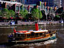 People cruising in steamer on Yarra River, with Southbank complex in background.