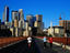 Women jogging across Stone Arch bridge with city skyline beyond.