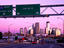 Traffic signs over highway with city skyline beyond at dusk.