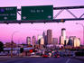 Traffic signs over highway with city skyline beyond at dusk.