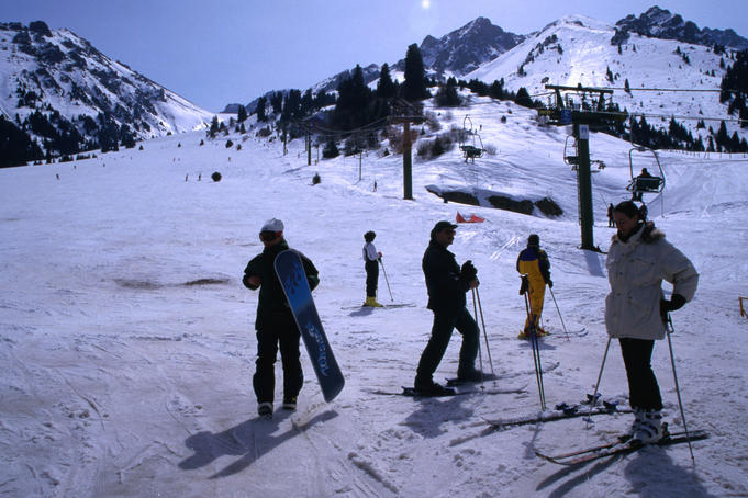 People with skis and snowboards at the bottom of a run on slopes of ski resort.